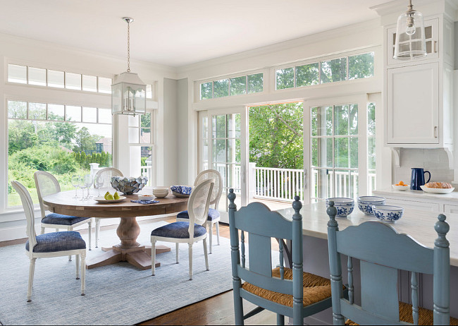 Benjamin Moore Gray Owl Kitchen and Breakfast Nook. Eat in kitchen features a Restoration Hardware Round Salvaged Wood Trestle Dining Table lined with white Vintage French Round Cane Back Fabric Side Chairs accented iwth blue seat cushions atop a blue rug illuminated by a white pagoda lantern surrounded by windows and doors. Digs Design Company.