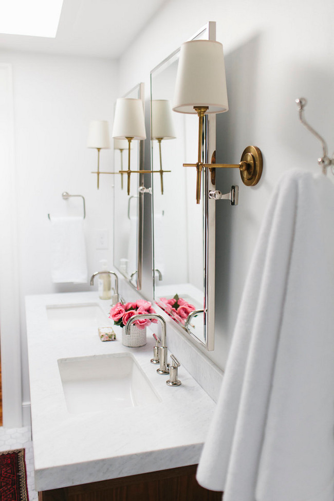 Bathroom. This bathroom boasts a freestanding walnut dual vanity topped with white marble fitted with his and hers sinks and Kohler Purists Faucets under Restoration Hardware Lugarno Traditional Pivot Mirror illuminated by Thomas O'Brien Bryant Sconces in Hand Rubbed Antique Brass. Shea McGee Design.