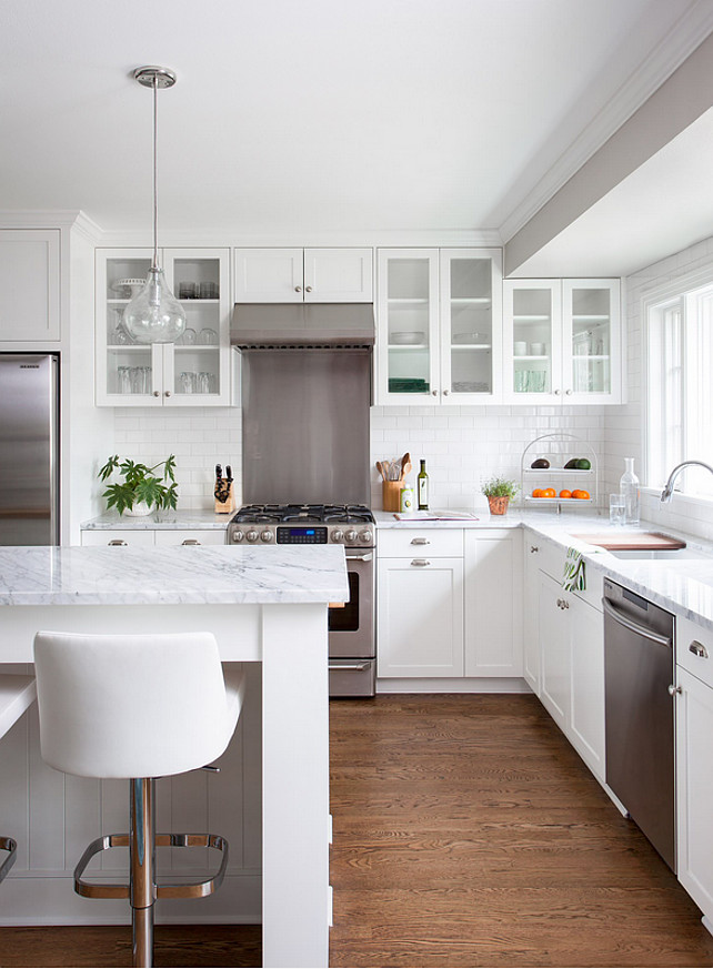 This small family home kitchen features 3cm Bianco Carrara Marble counters, hardware salvaged from original kitchen, a mixture of new and old oak flooring, Rittenhouse 3x6 white gloss tile for the backsplash, Benjamin Moore Simply White paint on the ceiling, BM Revere Pewter on the walls, and a clear Shades of Light Teardrop Seeded Pendant above the island.