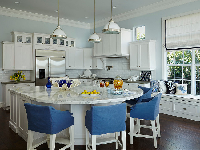 Blue and white Kitchen. In this blue and kitchen, Lee Industries stools surround the Carrara marble island top, refinished by Mario Ferazzoli & Son. Samuel & Sons tape outlines the Roman shades in Duralee fabric. Wellborn Cabinet’s cabinetry from DeStefano Designs and Restoration Hardware pendants already existed in the home.