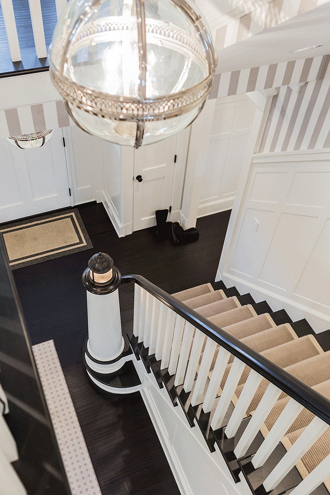 Foyer. Staircase Runner. Foyer features upper walls clad in white and gray stripe wallpaper and lower walls clad in board and batten which extends to the staircase with lighthouse banister light lined with a bound sisal rug illuminated by a Restoration Hardware Victoria Hotel Pendant. #Foyer #Staircase #StaircaseRunner Brookes and Hill Custom Builders