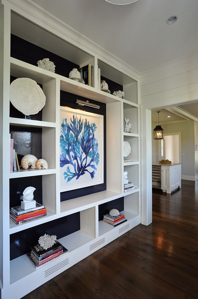 Built-in cabinet. Living Room Built-in Display Cabinet. Living Room with custom Built-in Display Cabinet. The living room features a custom built-in display cabinet just before entering the kitchen area. Notice the large seaweed art print against the dark glossy navy blue backdrop, lit by a library wall sconce. The shelves display stacked books, coral and seashells. #LivingRoom #Cabinet #Builtin #DisplayCabinet #Bookshelves #Bookcase Nina Liddle Design.