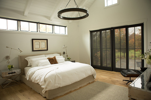 Clerestory Windows. Bed under Clerestory Windows. Industrial bedroom features paneled vaulted ceiling accented with a Ralph Lauren Roark Modular Ring Chandelier hanging over a natural linen slipcovered bed dressed in soft white linens placed under a row of clerestory windows flanked by metal x based nightstands illuminated by swing arm sconces.. #Clerestory #Window #Bedroom Hahn Builders.