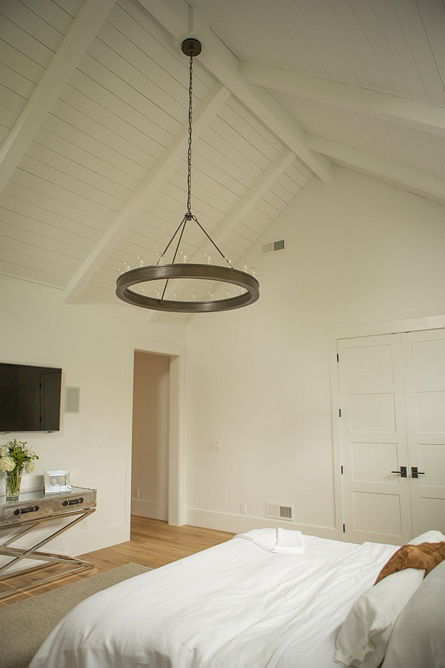 Bedroom Ceiling. Bedroom Lighting. This bedroom features paneled vaulted ceiling accented with a Ralph Lauren Roark Modular Ring Chandelier hanging over a bed dressed in soft white linens facing a metal x based console table with drawers adorned with leather strap pulls under a flatscreen TV. #Bedroom Hahn Builders.