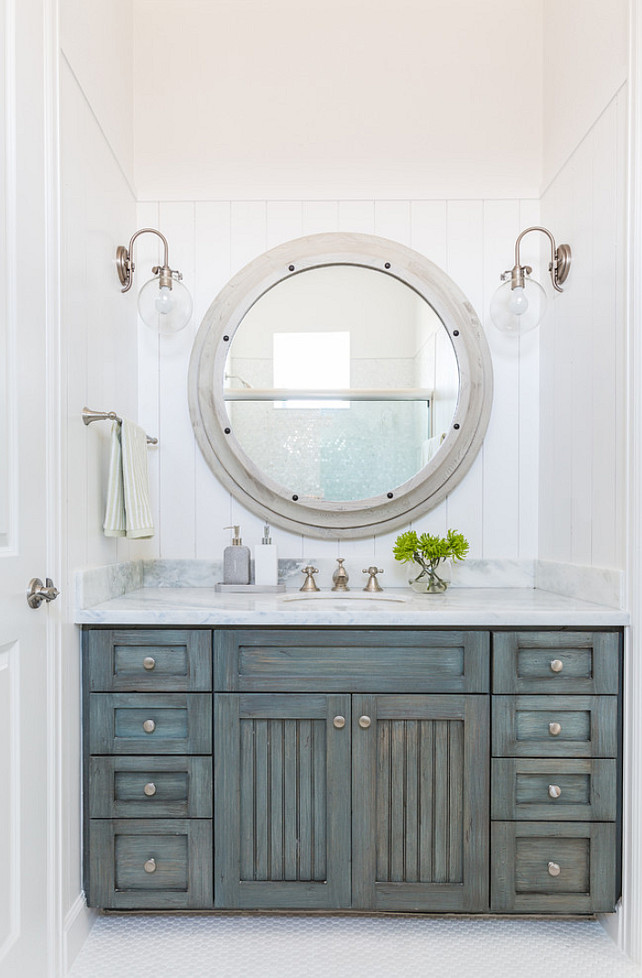 Distressed Bathroom Cabinet. This bathroom features vertical shiplap walls lined with a large gray wood mirror illuminated by clear glass barn sconce over a gray distressed washstand topped with white marble fitted with an oval sink and satin nickel faucet. #Bathroom #Distressed #Cabinet Laura U, Inc. 
