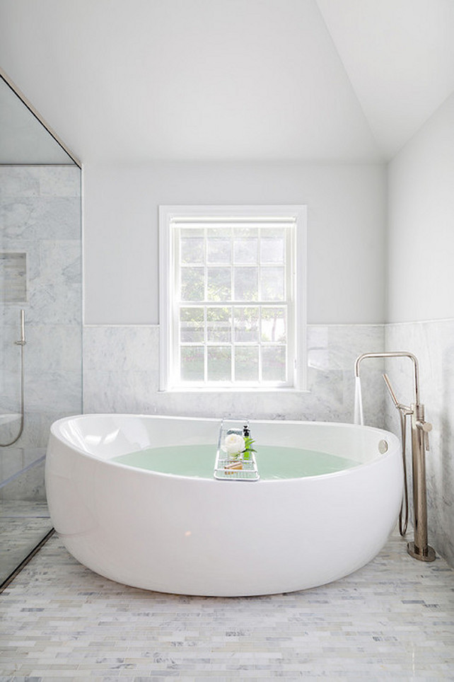 Bathroom. White and gray bathroom features upper walls painted gray and lower walls clad in marble wainscoting finished with marble pencil tiles alongside an egg shaped bathtub paired with floor mounted tub filler placed below window atop marble linear floor tiles which seamlessly continue into the walk-in shower. Clean Design Partners