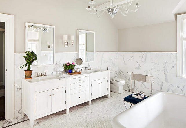 Bathroom. Bathroom ideas. Bathroom flooring ideas. Bathroom tiling ideas. The master bathroom features greige paint on upper walls and marble tiles on lower walls accented with marble pencil rail framing. The "Visual Comfort Lighting George II Chandelier" illuminates freestanding bathtub paired with polished chrome chair with blue velvet tufted cushion. Bathroom marble. #Bathroom Alisberg Parker Architects.