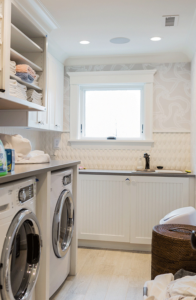 Beadboard Cabinets in laundry Room. Laundry Room Beadboard cabinets. Laundry Room Beadboard cabinets and wallpaper. The laundry room features half wall covered in rope knot wallpaper and the other part are covered in 3D Tiles. White beadboard cabinets were topped with gray quartz countertop which frames the laundry sink. This room also boasts open shelving, closed cabinets and Beachwood Porcelain Tiles. #LaundryRoom #Beadboard #cabinets Brookes and Hill Custom Builders.