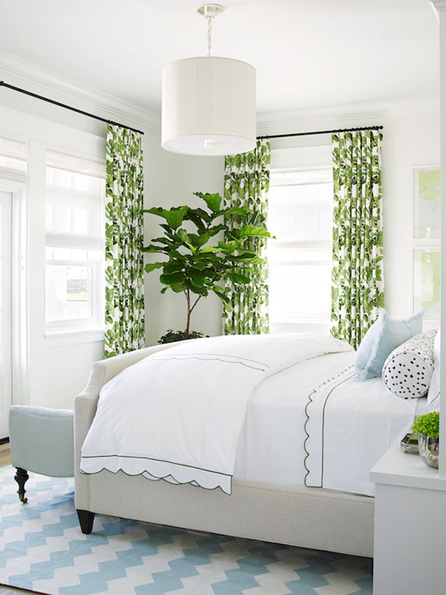 Bedroom Decor. Coastal bedroom features light gray bed dressed in scalloped duvet and shams, pillow upholstered in Brunschwig & Fils Les Touches Cotton Print Black Fabric and sky blue lumbar pillow atop white and blue chevron rug alongside a sky blue bench placed at the foot of the bed across from fiddle leaf fig plant flanked by windows dressed in Peter Dunham Fig Leaf Fabric curtains illuminated by a Barbara Barry Perfect Pleat Pendant. #bedroomDecor 