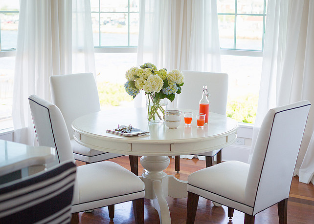 Breakfast Nook. Beautiful breakfast nook fills bay window dressed in white cotton drapes with a Cornice Hanging Lantern mounted over a white pedestal dining table lined with white dining chairs with black piping. #BreakfastNook