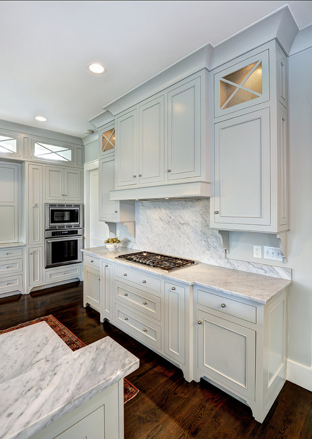  Kitchen Countertop & Backsplash Combo. Gray kitchen backsplash and countertop ideas. Incredible kitchen with wall and cabinetry painted light gray, Benjamin Moore Gray Owl. The pale gray cabinets are accented with nickel hardware and finished with Carrera Marble countertops with a Carrera Marble cooktop backsplash. The integrated stove top pairs with a disguised oven hood hidden behind cabinet doors which are flanked by glass front accent cabinets. A stainless steel double oven stands at the far end of the kitchen framed by a wall of built-in cabinetry.