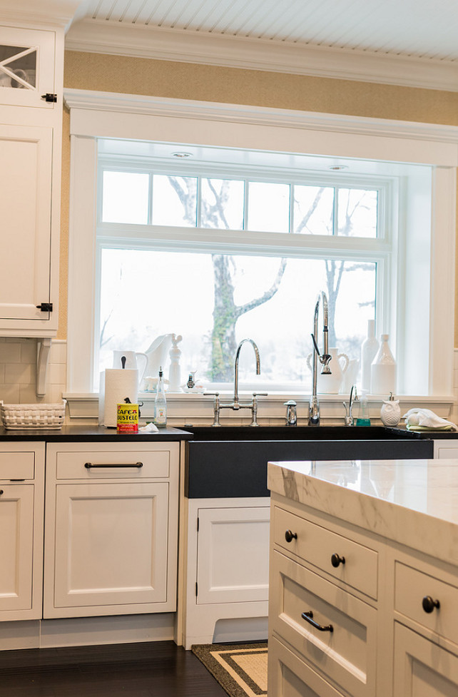 Kitchen sink with two faucets. #Kitchen #Sink #Faucets A transitional black apron sink is paired with a bridge gooseneck faucet and a pull-out spray faucet. The kitchen island is topped with thick marble countertop contrasting with espresso hardood floors. Brookes and Hill Custom Builders.