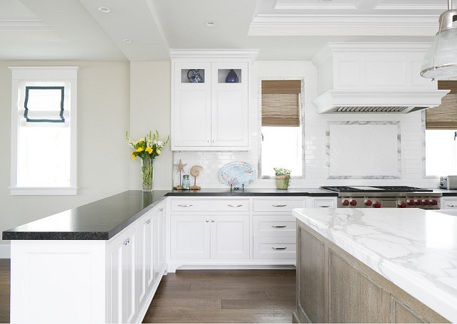 Kitchen with gray countertop, pendant lights, recessed lighting, shells, starfish, coastal decor, white cabinets, white kitchen, white marble countertop, white tiles, wood floor.