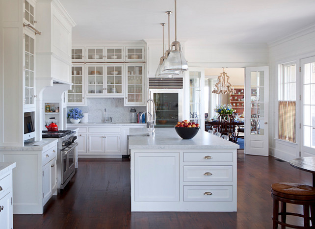 Kitchen. Coastal White Kitchen. Coastal White Kitchen Cabinet. White Coastal kitchen with tall glass cabinets. Large kitchen with glass-front upper cabinets and inset lower cabinets paired with white marble countertops and white marble slab backsplash next to glass-front refrigerator. #CoastalKitchen #CoastalKitchenDesign #WhiteCoastalKitchen Jeannie Balsam LLC.