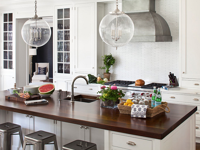 Kitchen. Kitchen Ideas. Kitchen Cabinet. White kitchen with butcher's block countertop island. The kitchen features creamy white cabinets paired with white marble countertop and white linear tiled backsplash flanking stainless steel, dome hood over Wolf Range. Globe glass pendants hang over butcher block island with sink and satin nickel gooseneck faucet lined with Tolix Barstools. #Kitchen Alisberg Parker Architects.