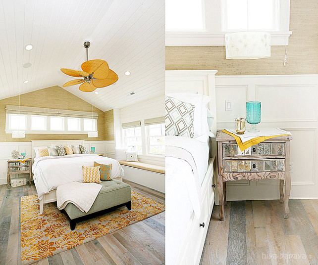 Master Bedroom. Bedroom design with sand grasscloth wallpaper, wall panels, sunburst mirror, mustard yellow sliding barn door, beadboard ceiling, white wood bed, gray tufted bench, mirrored nightstands and built-in window seat.