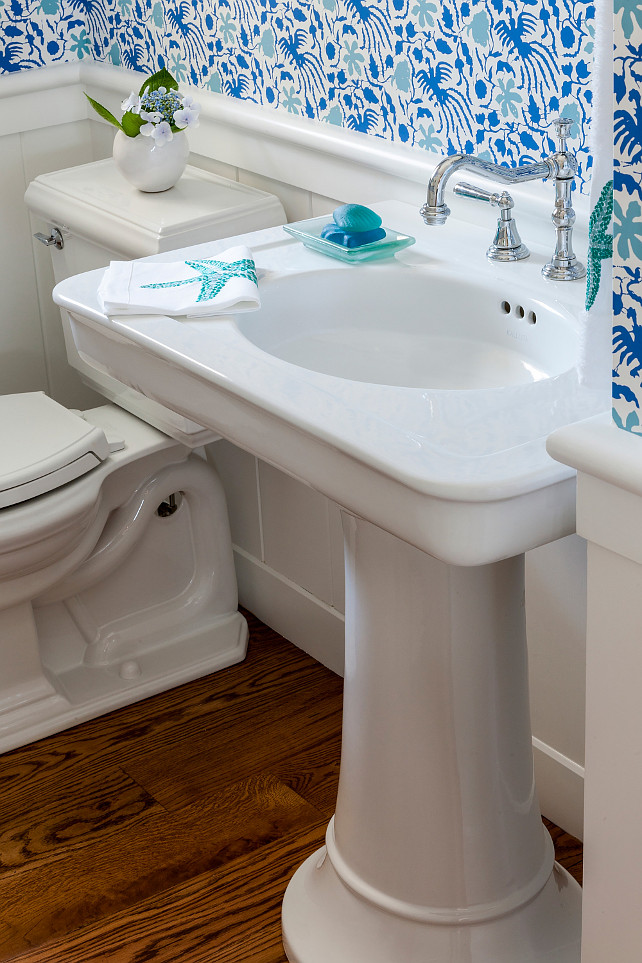 Powder room. Coastal Powder Room with pedestal sink and white and blue wallpaper. The powder room features hardwood flooring, pedestal sink, wall paneling and a blue and white wallpaper. #Powderroom SLC Interiors.